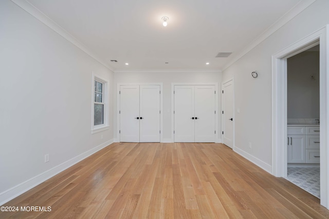 unfurnished bedroom featuring crown molding, two closets, connected bathroom, and light hardwood / wood-style floors