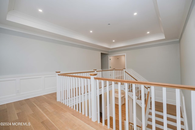 hall featuring ornamental molding, light hardwood / wood-style flooring, and a raised ceiling