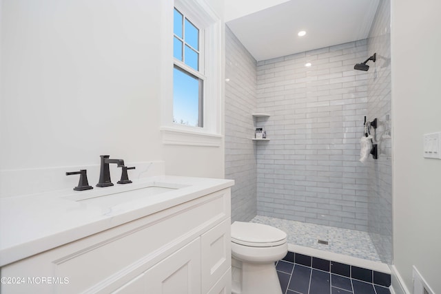 bathroom with a tile shower, vanity, tile patterned flooring, and toilet