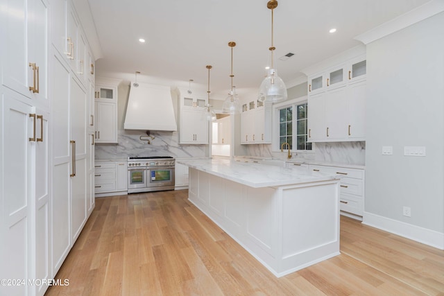 kitchen with pendant lighting, premium range hood, white cabinetry, range with two ovens, and light wood-type flooring