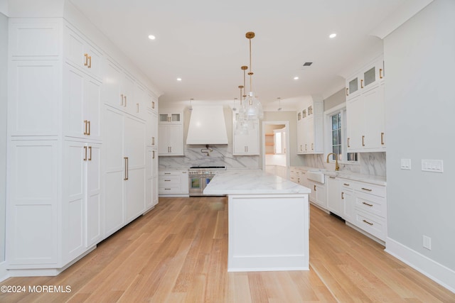 kitchen with premium range hood, white cabinetry, light hardwood / wood-style floors, and high end stainless steel range oven