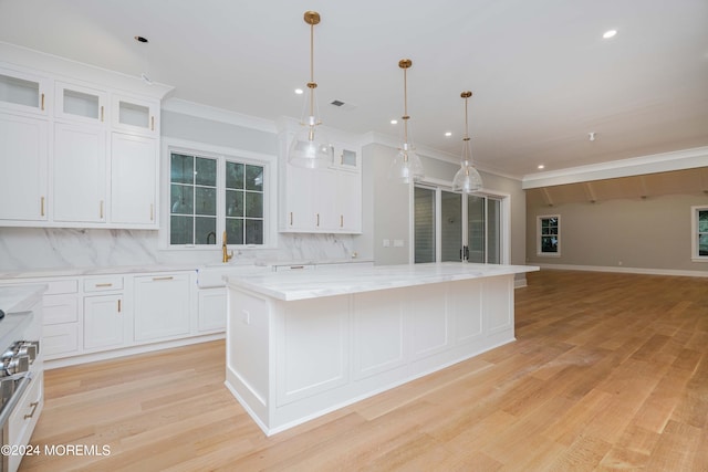 kitchen with white cabinets, a kitchen island, decorative light fixtures, backsplash, and light hardwood / wood-style flooring