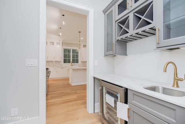 kitchen featuring gray cabinets, beverage cooler, light hardwood / wood-style flooring, sink, and light stone counters