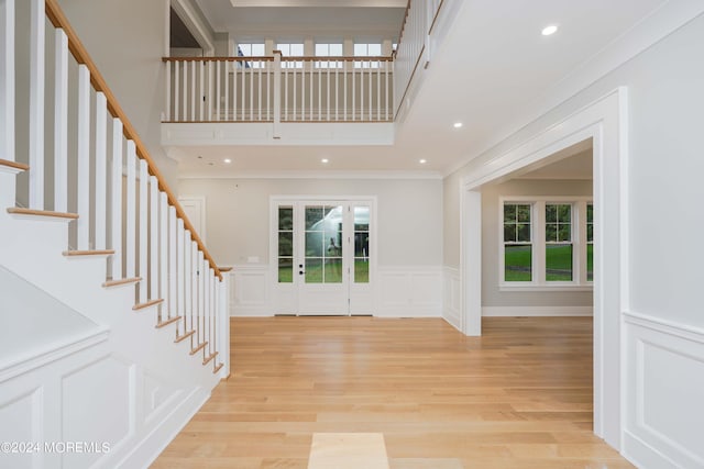 foyer with plenty of natural light, crown molding, and light wood-type flooring