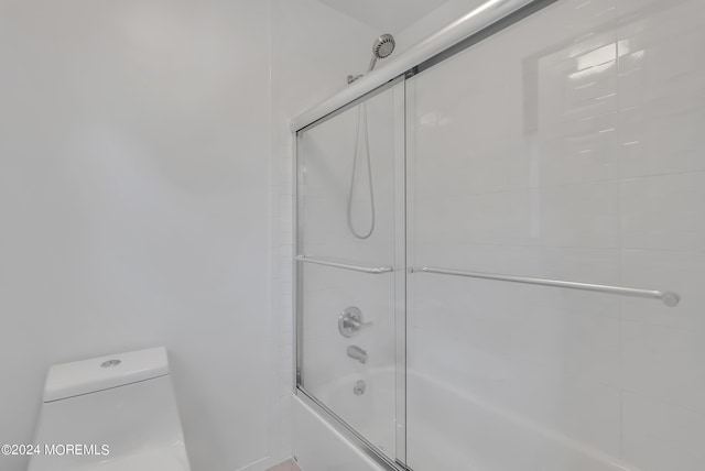 bathroom featuring toilet and bath / shower combo with glass door