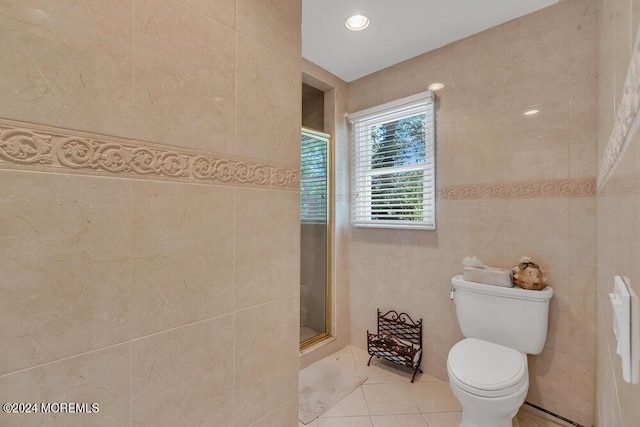 bathroom featuring tile patterned floors, toilet, tile walls, and a shower with shower door