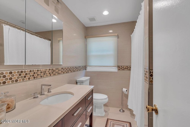 bathroom with toilet, vanity, tile patterned floors, and tile walls