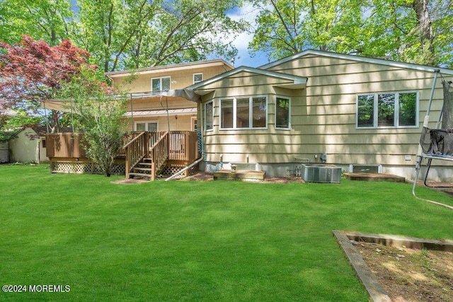 rear view of property featuring a yard, a trampoline, central AC, and a deck