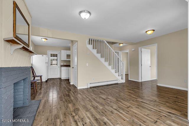 unfurnished living room with hardwood / wood-style floors, a brick fireplace, and a baseboard radiator