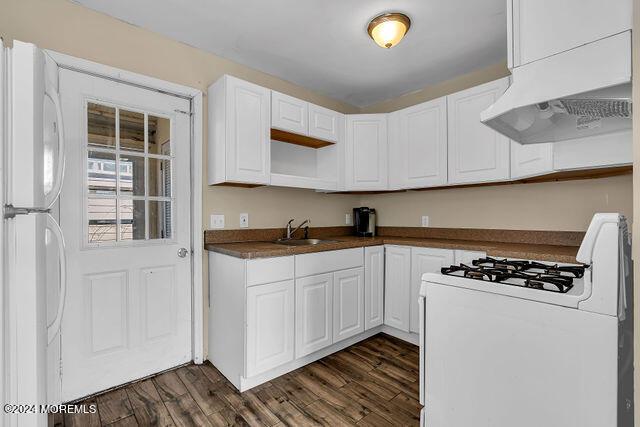 kitchen featuring dark hardwood / wood-style flooring, premium range hood, white appliances, sink, and white cabinets