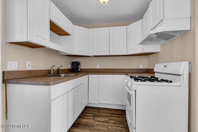 kitchen with white cabinetry, dark hardwood / wood-style flooring, white gas range, and sink