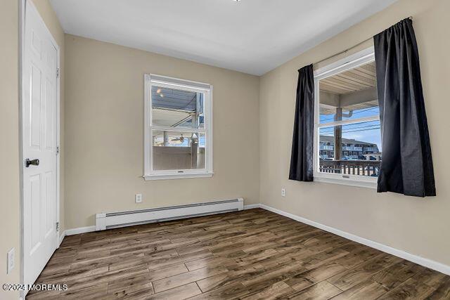 unfurnished room with dark hardwood / wood-style flooring and a baseboard heating unit