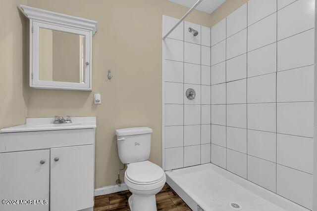 bathroom with a tile shower, vanity, wood-type flooring, and toilet