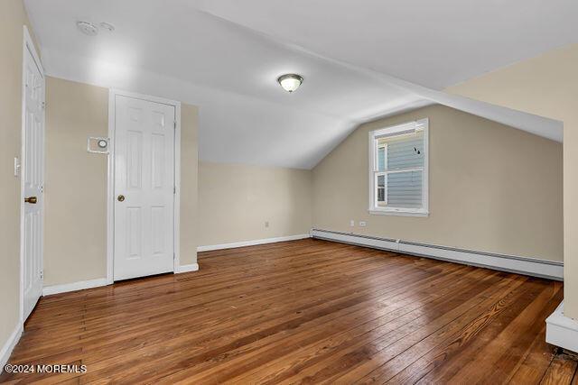 additional living space featuring dark hardwood / wood-style flooring, vaulted ceiling, and a baseboard heating unit