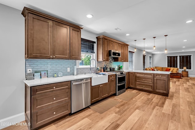 kitchen featuring light hardwood / wood-style floors, kitchen peninsula, appliances with stainless steel finishes, sink, and pendant lighting