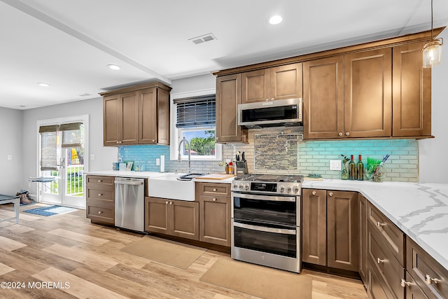 kitchen with decorative light fixtures, light hardwood / wood-style floors, tasteful backsplash, appliances with stainless steel finishes, and sink