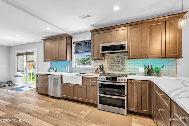 kitchen featuring appliances with stainless steel finishes, decorative light fixtures, light hardwood / wood-style floors, backsplash, and sink