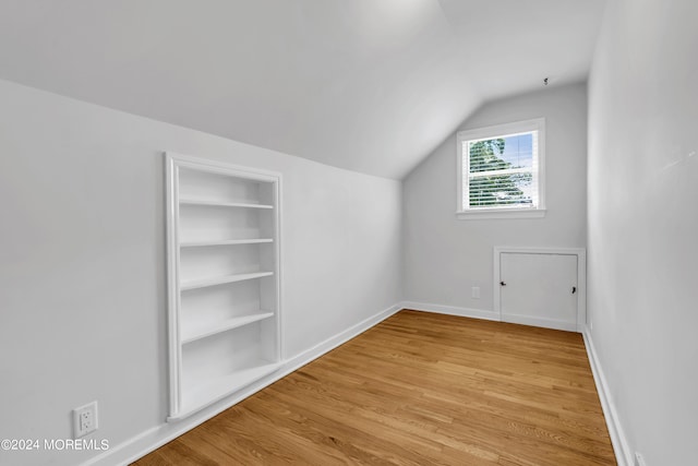 additional living space with vaulted ceiling, built in shelves, and light hardwood / wood-style flooring