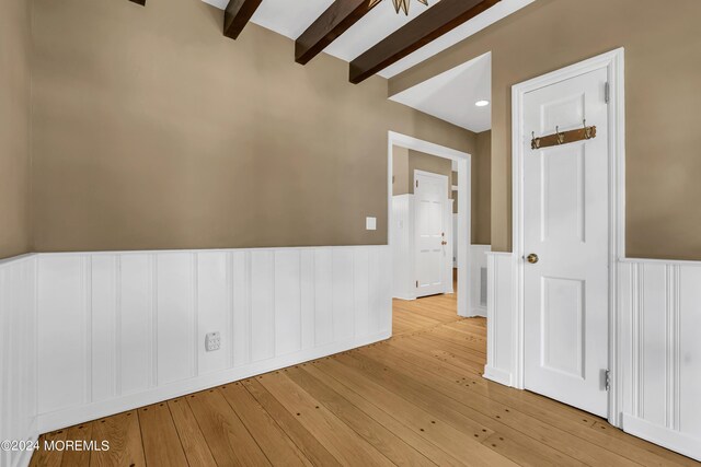 unfurnished room featuring light hardwood / wood-style floors and beam ceiling