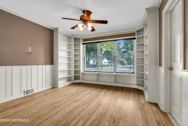 empty room featuring ornamental molding, built in shelves, ceiling fan, and light hardwood / wood-style flooring