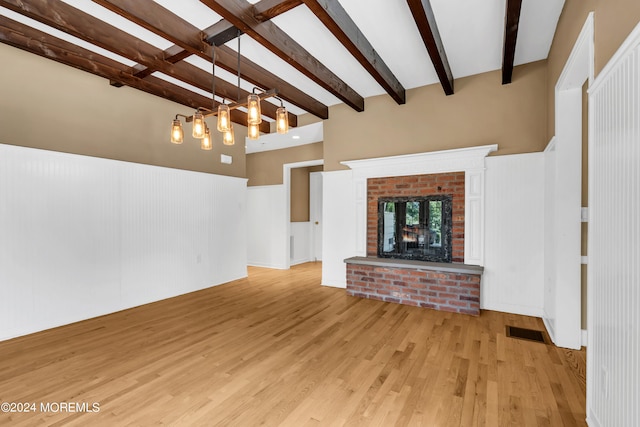 unfurnished living room with beamed ceiling, light hardwood / wood-style floors, and a brick fireplace