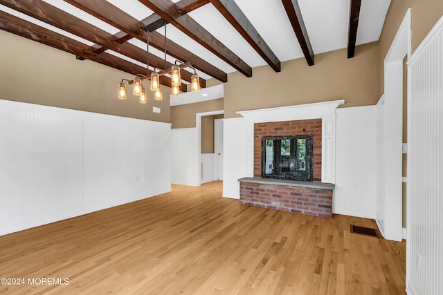 unfurnished living room with beam ceiling, light wood-type flooring, and a brick fireplace