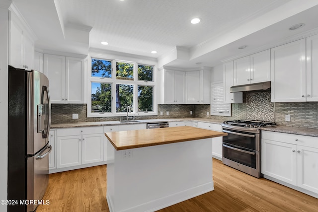 kitchen with stainless steel appliances, a kitchen island, wood counters, and light hardwood / wood-style flooring