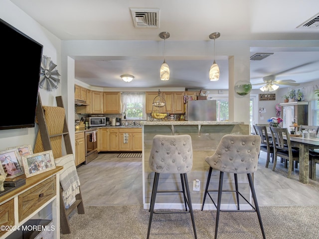 kitchen with light stone counters, light tile flooring, a kitchen breakfast bar, ceiling fan, and appliances with stainless steel finishes