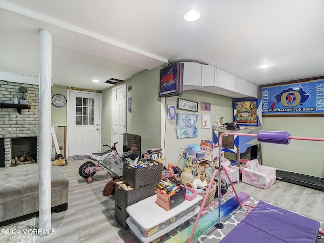 playroom featuring a fireplace, brick wall, and light hardwood / wood-style flooring