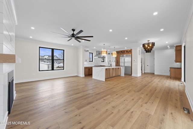 unfurnished living room featuring light hardwood / wood-style flooring, sink, a large fireplace, crown molding, and ceiling fan with notable chandelier