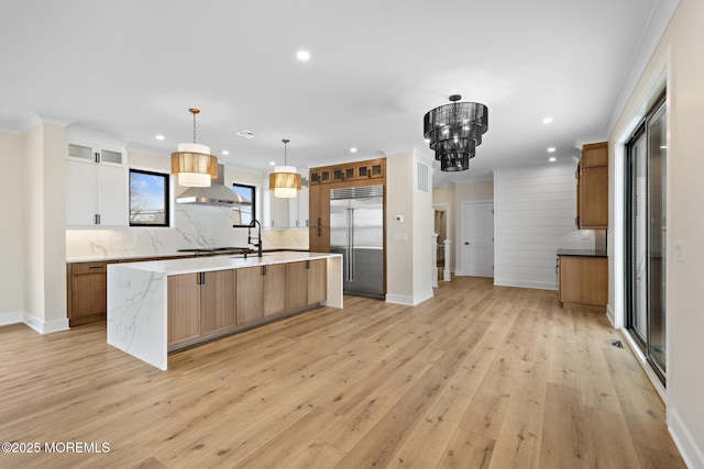 kitchen featuring light wood-type flooring, hanging light fixtures, a spacious island, stainless steel built in refrigerator, and white cabinets