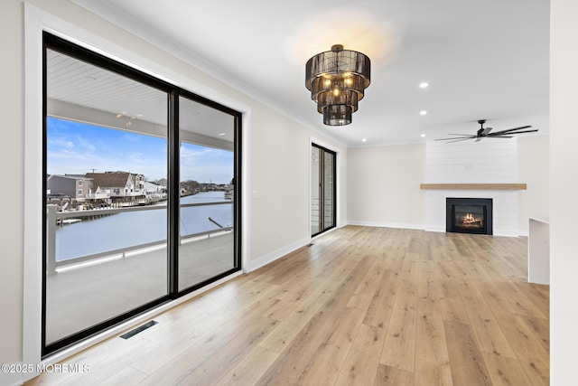 unfurnished living room with a water view, crown molding, a large fireplace, and light hardwood / wood-style floors