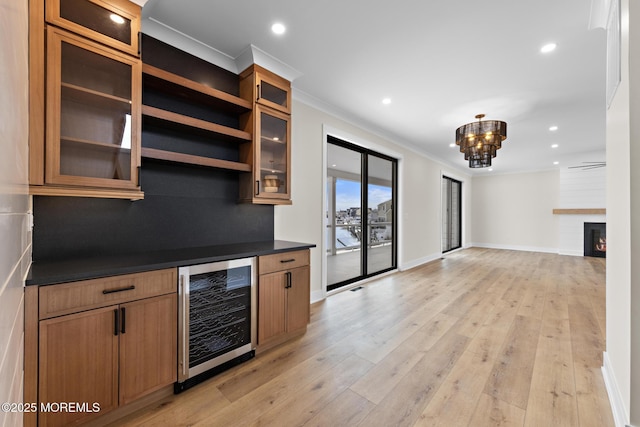 kitchen with a large fireplace, light hardwood / wood-style floors, crown molding, an inviting chandelier, and wine cooler