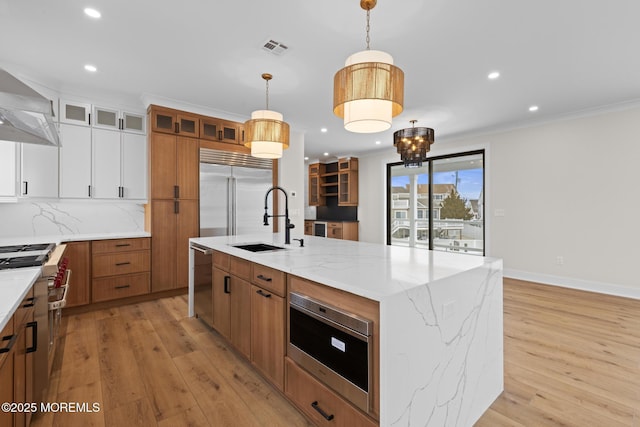 kitchen featuring built in appliances, sink, white cabinetry, decorative light fixtures, and an island with sink