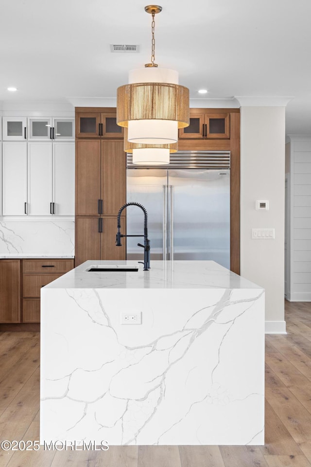 kitchen with stainless steel built in refrigerator, hanging light fixtures, white cabinets, light hardwood / wood-style floors, and sink