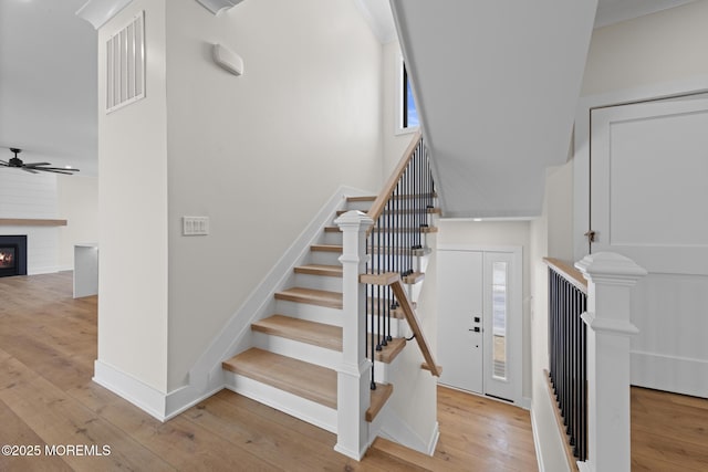 stairs with a fireplace, hardwood / wood-style flooring, a towering ceiling, and ceiling fan