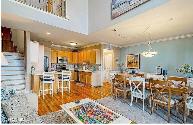 dining space featuring crown molding, light wood-type flooring, and a towering ceiling