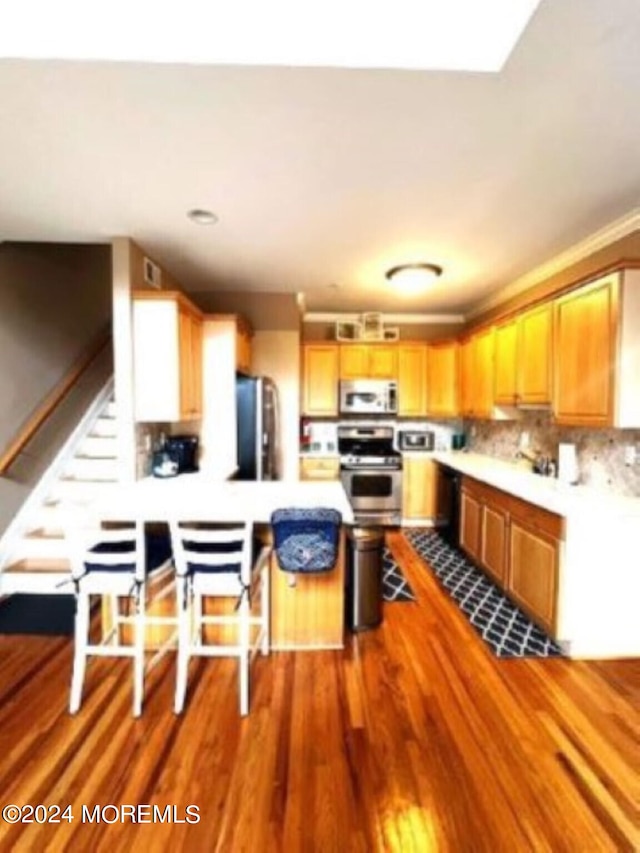 kitchen featuring stove, hardwood / wood-style floors, kitchen peninsula, stainless steel refrigerator, and backsplash