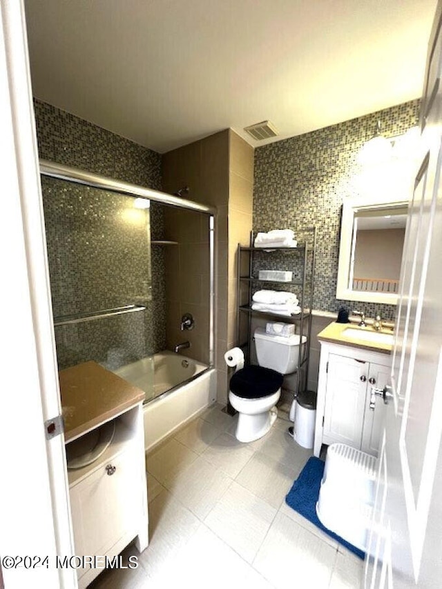 full bathroom with combined bath / shower with glass door, tile patterned flooring, tile walls, toilet, and vanity