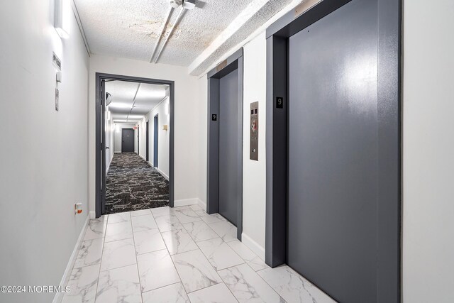 corridor with a textured ceiling, elevator, and light tile patterned floors