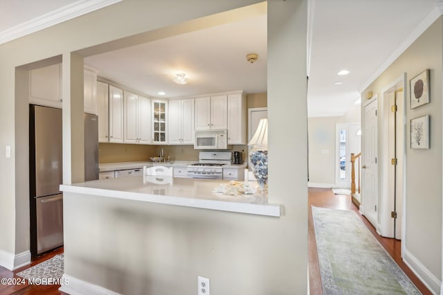 kitchen featuring hardwood / wood-style floors, white appliances, white cabinets, crown molding, and kitchen peninsula