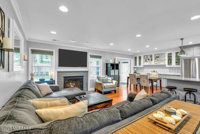 living area with ornamental molding, light wood-style floors, recessed lighting, and a warm lit fireplace