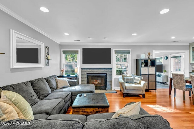 living room with light wood-type flooring, a fireplace, recessed lighting, and ornamental molding