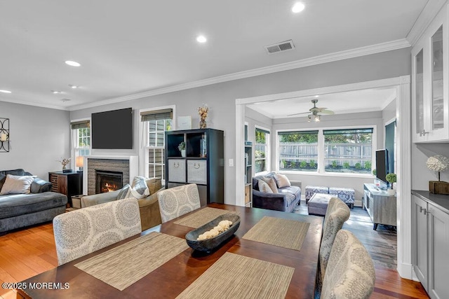 living area with recessed lighting, wood finished floors, ceiling fan, crown molding, and a stone fireplace
