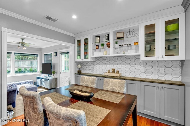 kitchen featuring dark countertops, crown molding, light wood-style floors, backsplash, and glass insert cabinets