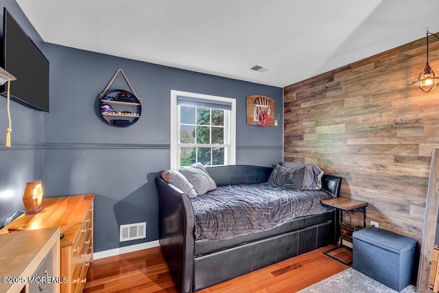 bedroom with wooden walls, an accent wall, and wood finished floors