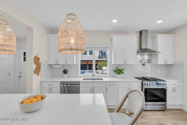 kitchen with stainless steel appliances, white cabinetry, hanging light fixtures, and wall chimney exhaust hood