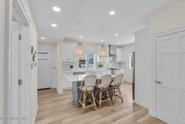 kitchen featuring white cabinetry, a kitchen breakfast bar, hanging light fixtures, a center island, and wall chimney exhaust hood