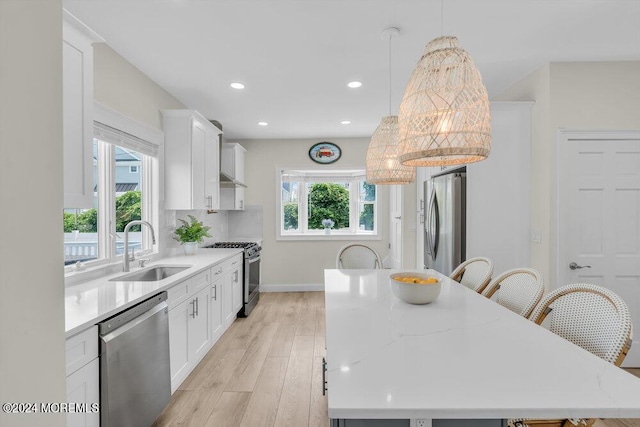 kitchen with appliances with stainless steel finishes, white cabinetry, sink, hanging light fixtures, and a center island