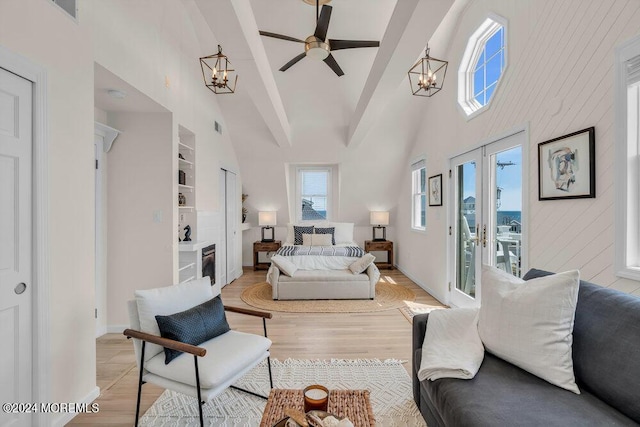 living room featuring french doors, built in shelves, light hardwood / wood-style flooring, a towering ceiling, and ceiling fan with notable chandelier